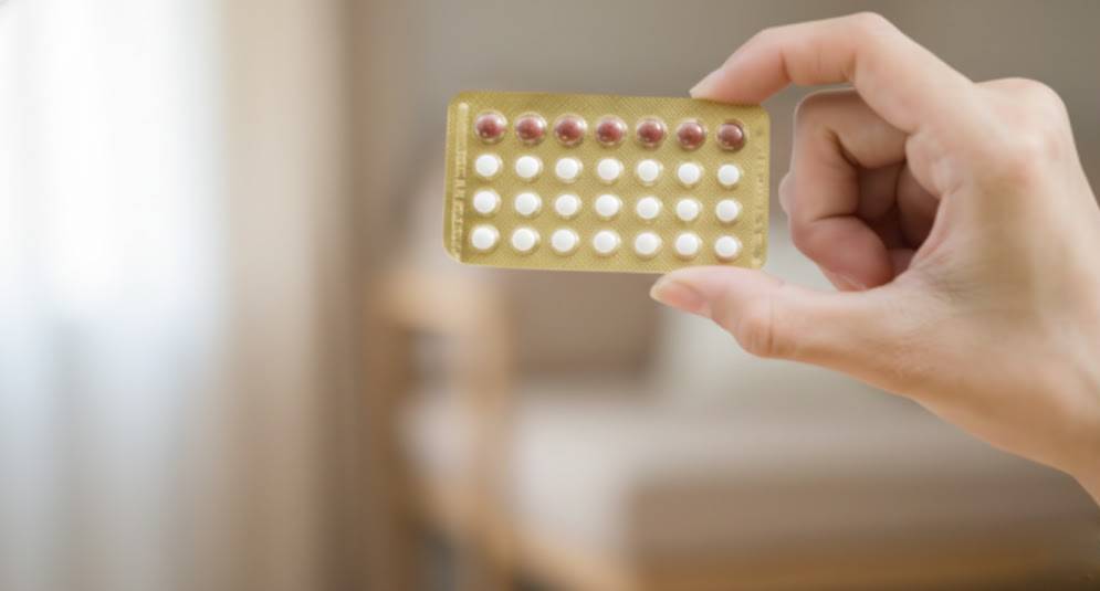 Mão de mulher a segurar uma cartela de pílulas contracetivas